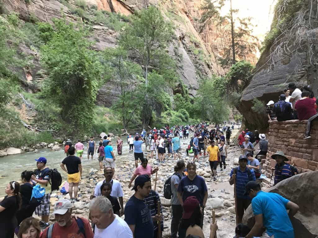 A very busy crowd of people gettting ready to hike the narrows in the summer on the rocks next to the water.
