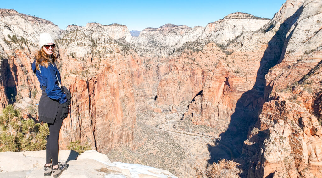 A woman stands on a ledge looking out at the beautiful Angel's Landing