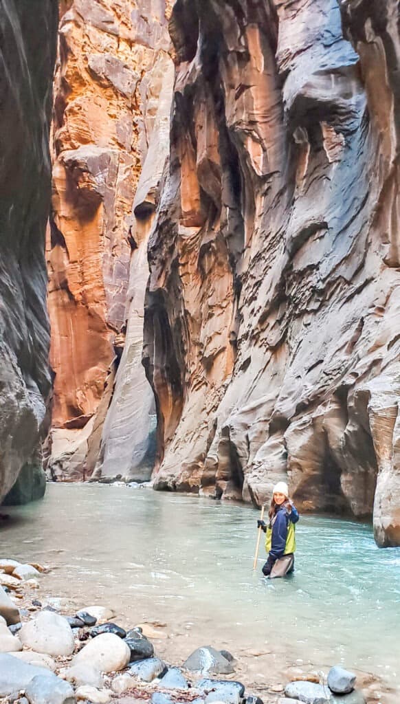 A woman looks back in the middle of the light blue stream leading throughout the slot canyon