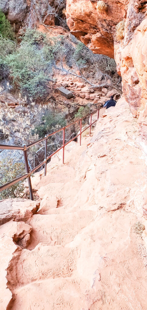 A stone path with lots of dirt and sand next to a railing right next to the large canyon.