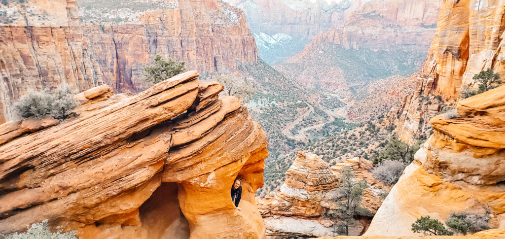 A man sits in the small curved rock in front of the stunning large valley with large, steep rock walls.
