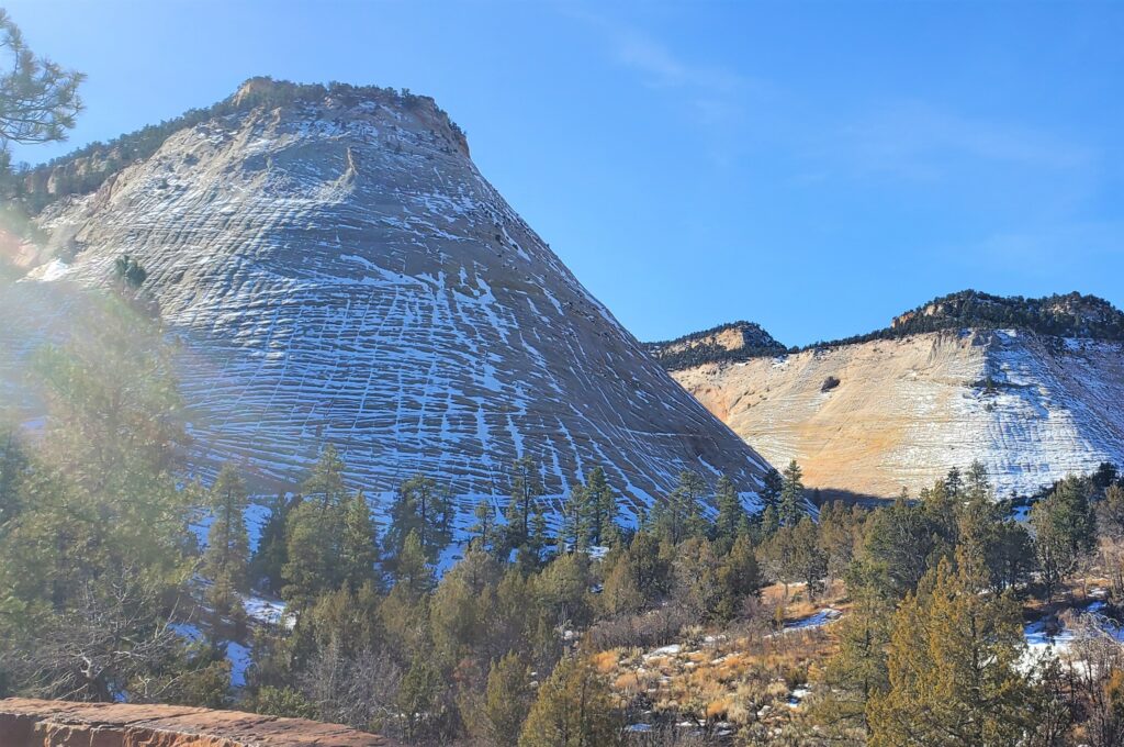A tall, slanted, cone like brown rock formation with snow covering the sides.