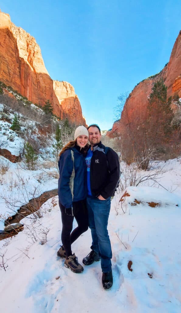 A man and woman stand on the snow in front of the path parrelel to the small stream in Taylor's Creek