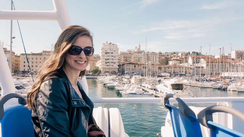 A woman sits in the back of a ferry with lots of boats in the background with lots of smaller faster boats being held in the port.