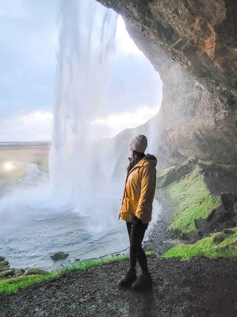 A woman stands in front of a waterfall that goes into a pool.