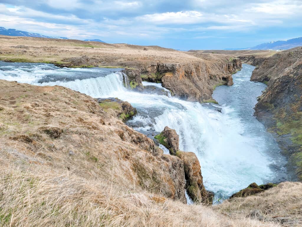 A waterfall cascades down multiole layers of rocks with white water and then continues down a river.