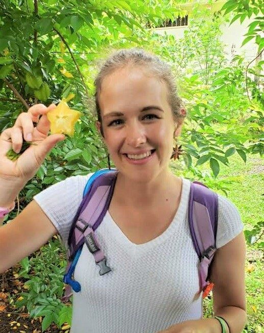 A smiling woman in a white shirt holds up a yellow fruit in the shape of a star for the camera.