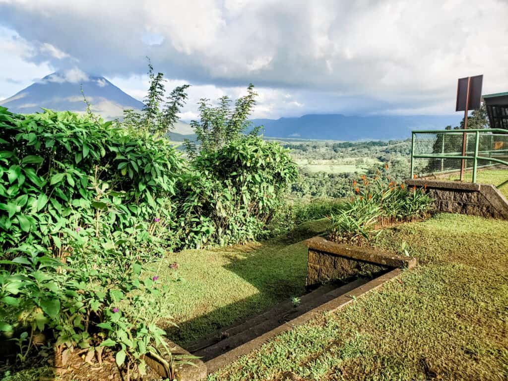 A stone staircase that leads to the final hanging bridge with mountains and a volcano in the backgruond.