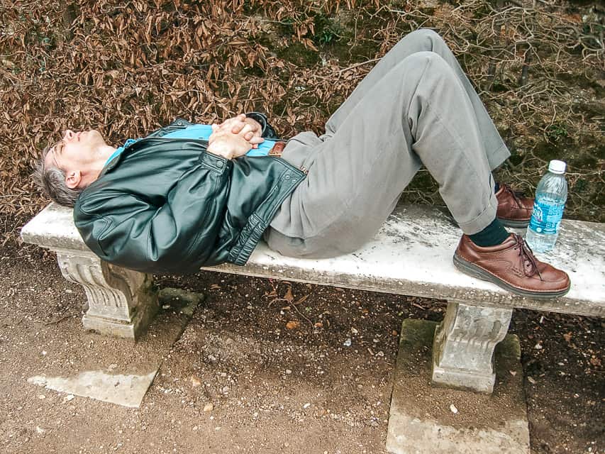 A man lies on a stone bench in agony.