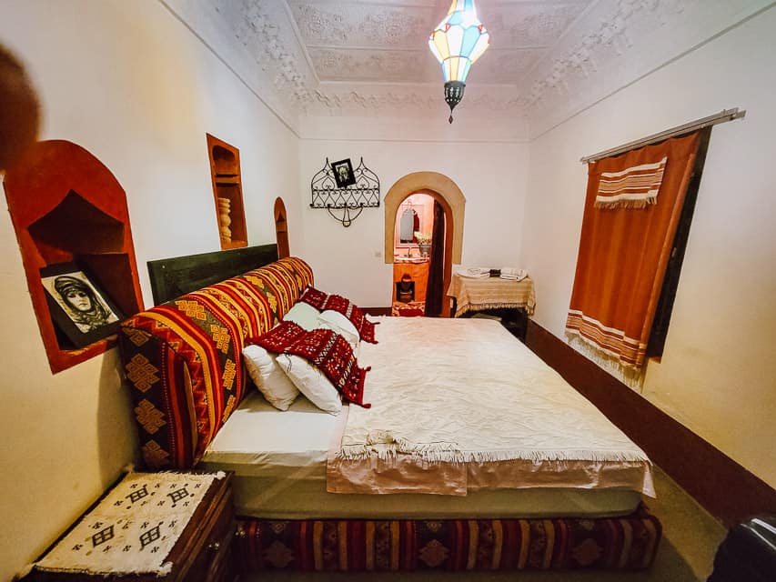 A colorful room in Tamellalt - with red and yellow accents on the curtains, headboard, covers, and in the bathroom.