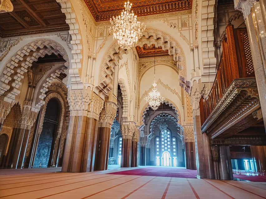 The inside of the Hassan II mosque has soaring ceilings, red and white carpets, grand chandeliers, carved cedarwood ceilings, and intricately hand-carved stucco arches.