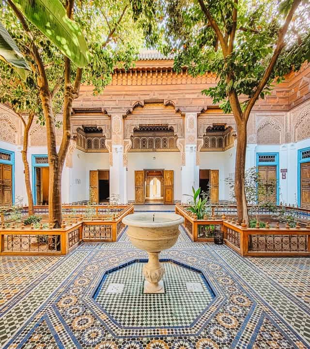 A small courtyard in the Bahia Palace, one of the most uniquely beautiful places in marrakech. There's a fountain in the middle of the room, colorful ceramics on the floor, trees growing in each quadrant, and dark cedarwood around the exterior of the room.