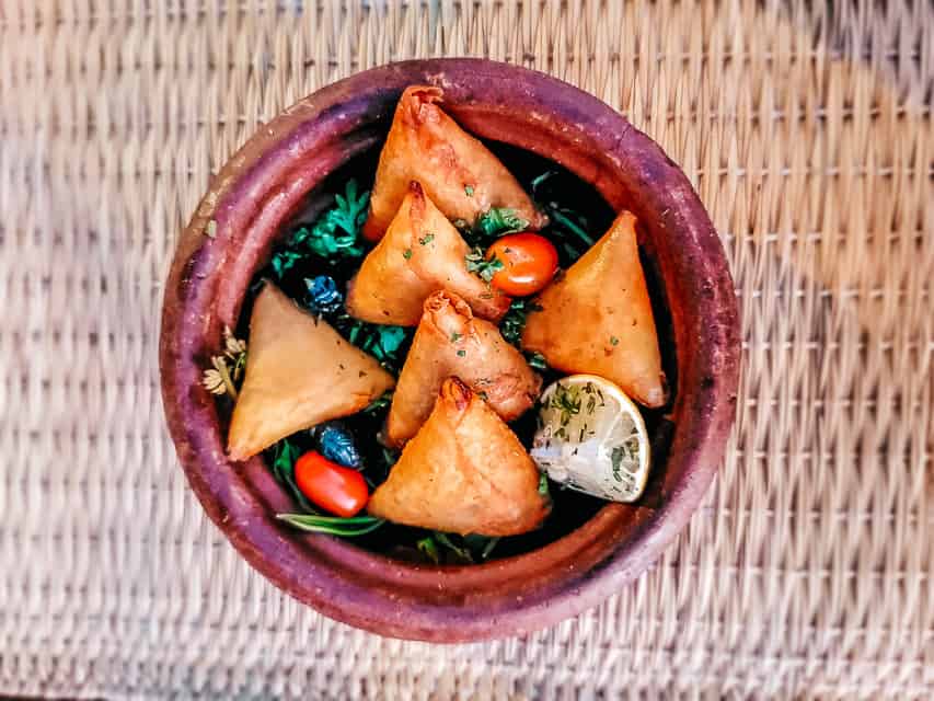6 triangle shaped fried pastries, called brouiats, sit in a earthenware bowl on a wicker mat in Marrakech.