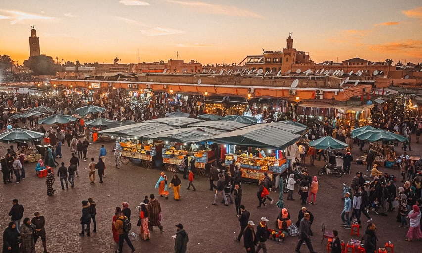 A view of the busy Jemma el-fna square at night, with many people wlaking through and stalls set up selling fruit and other things.