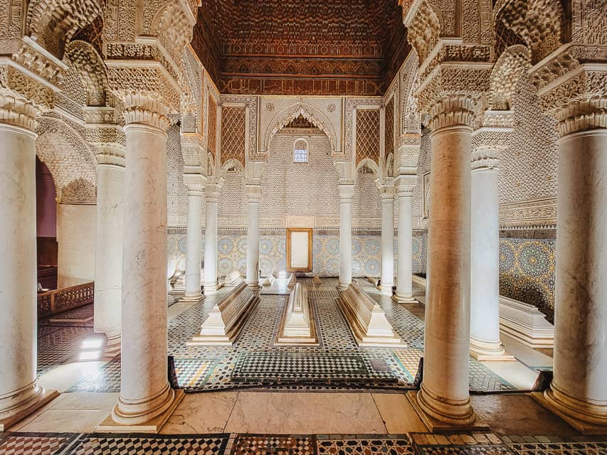 The Room of 12 Columns in the Saadian Tombs, which has carved stucco arches over 12 columns, carved cedarwood ceilings, and tiled floors, with several white markers over the tombs.