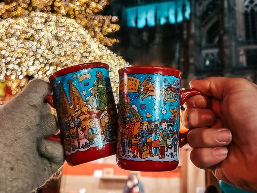 Two mugs from the Dom market held up in front of the sparkling Christmas tree.
