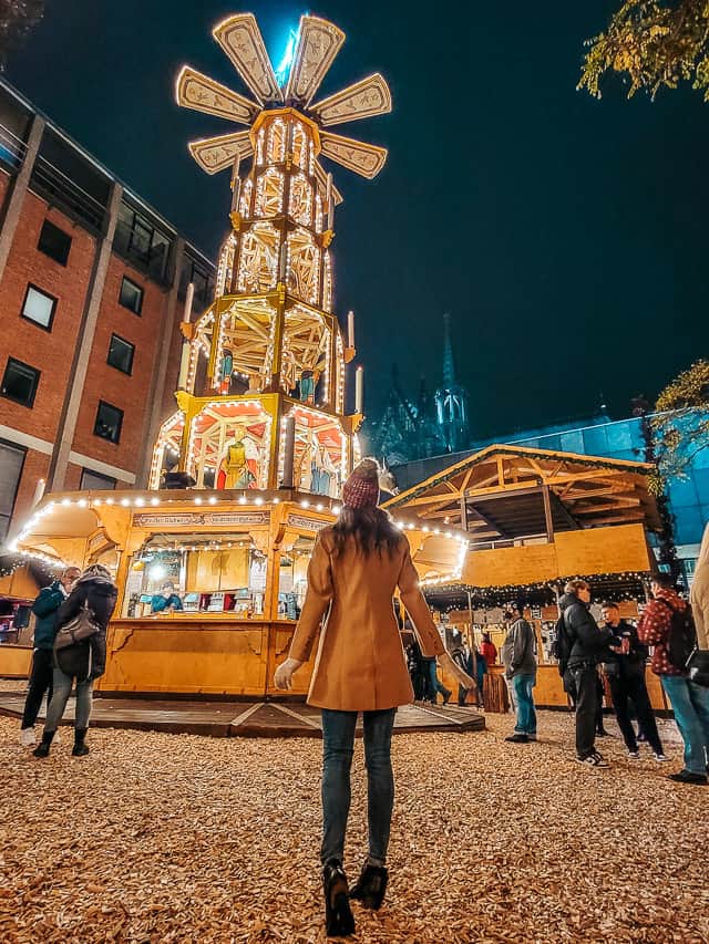 A tall tower with fan blades at the top is light up and has a little stand serving drinks underneath - this is a Christmas pyramid.