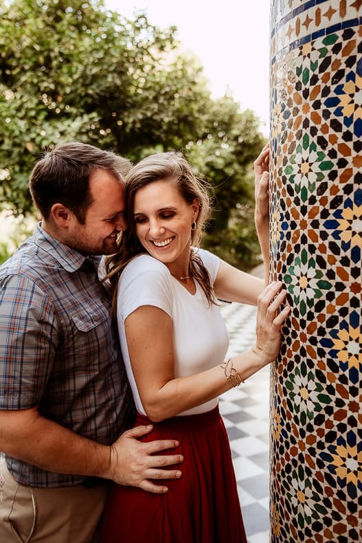 A man stands behind a woman and they smile at each other by a beautiful tiled column in Marrakech.