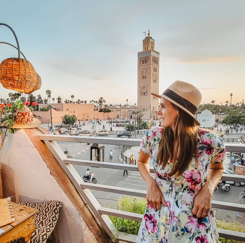 A woman sits on a rooftop terrace of a restaurant, looking over the Koutubia Mosque and minaret in Marrakech.