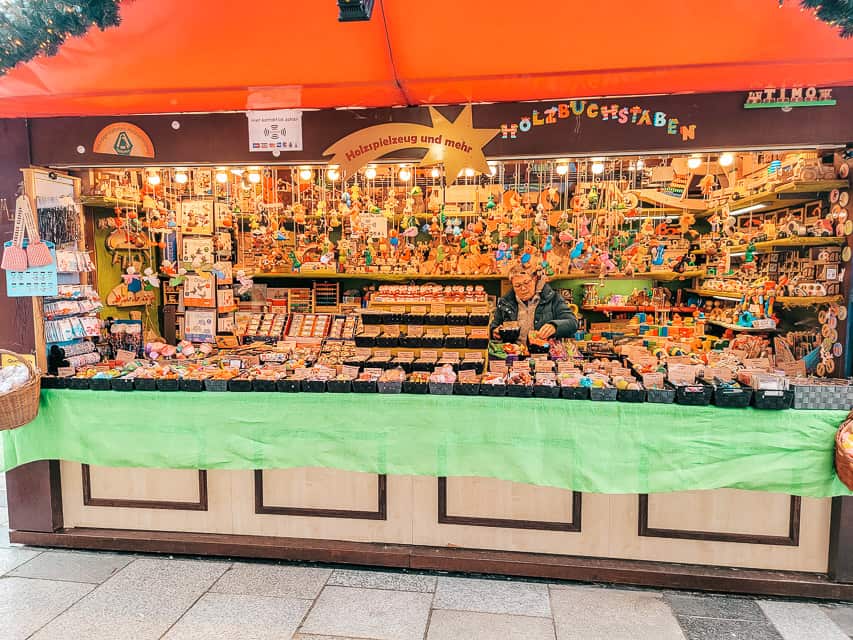 A stall of the Cologne Christmas market, with a red roof, a shooting star with the name of the stall in the middle, and the stall full of fun little toys for children.