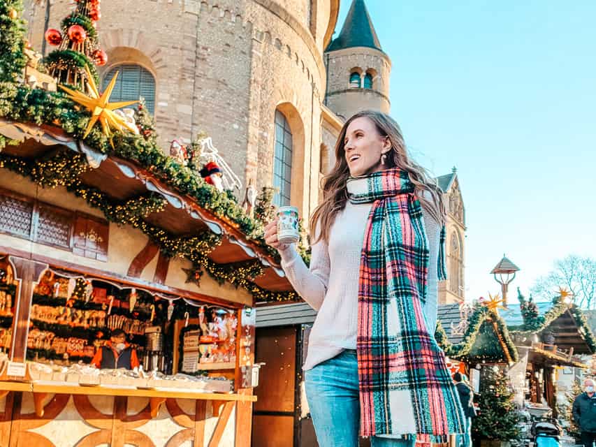 A smiling woman holds a mug with a drink in it and walks through the market in Trier.