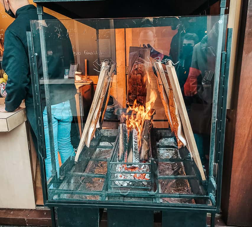 A small firepit encased in glass has salmon being grilled on wooden planks next to the flame.