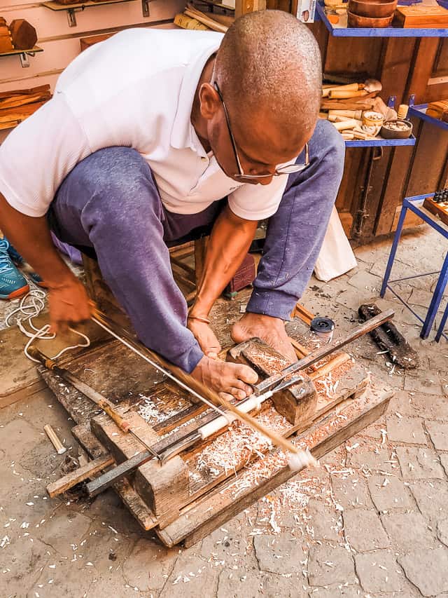 A Moroccan man works a contraption with his feet, creating a design in a hunk of wood.