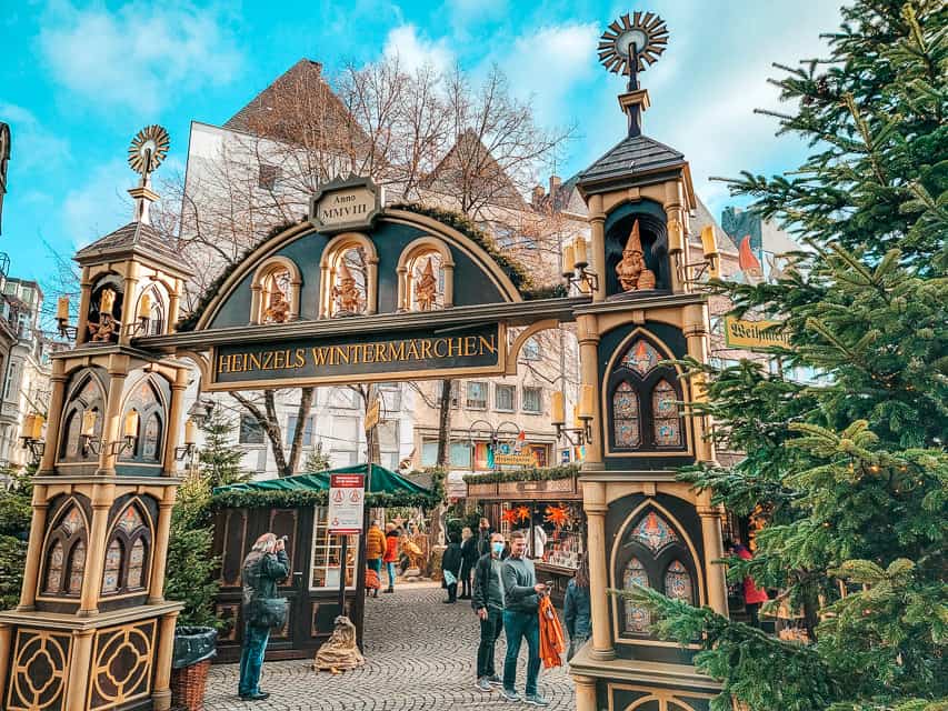 The entrance gate to the Heinzel's Wintermarchen christmas market in Cologne -pine trees to the side of the gate, and gnomes decorate the top and sides.
