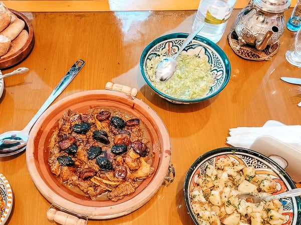 Chicken and prune tagine, roasted potatoes, and cucumber salad are served in colorful bowls.