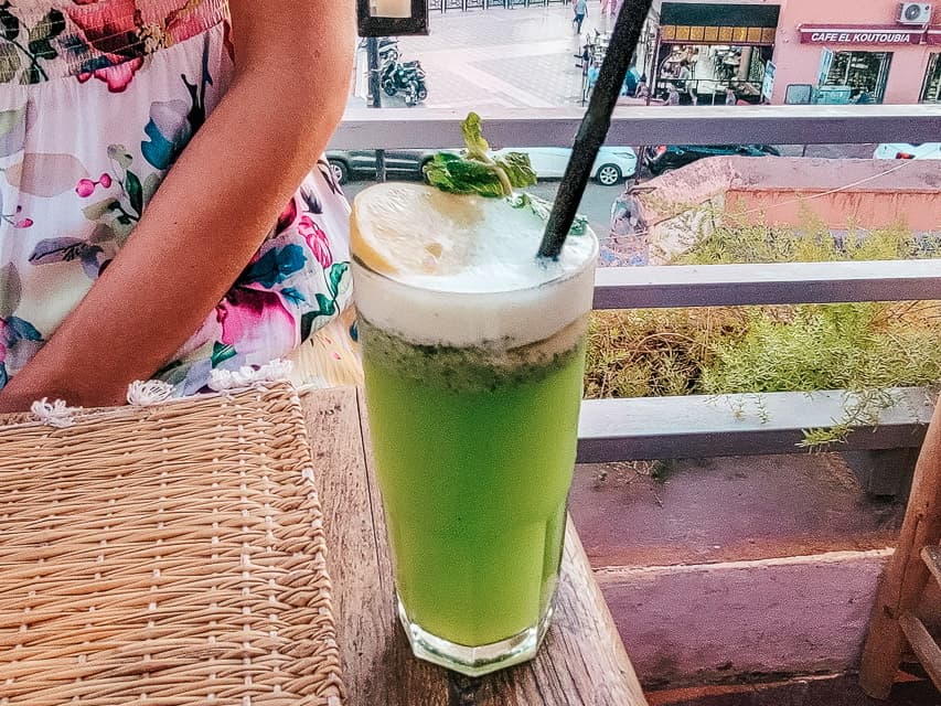 A glass with a green beverage - mint lemonade. It is frothy at the top and comes with a lemon slice.