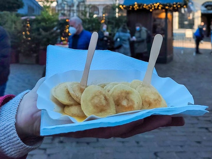 A hand holds a paper plate of pfannkuchen, which are small, soft and fluffy pancake-like treats.