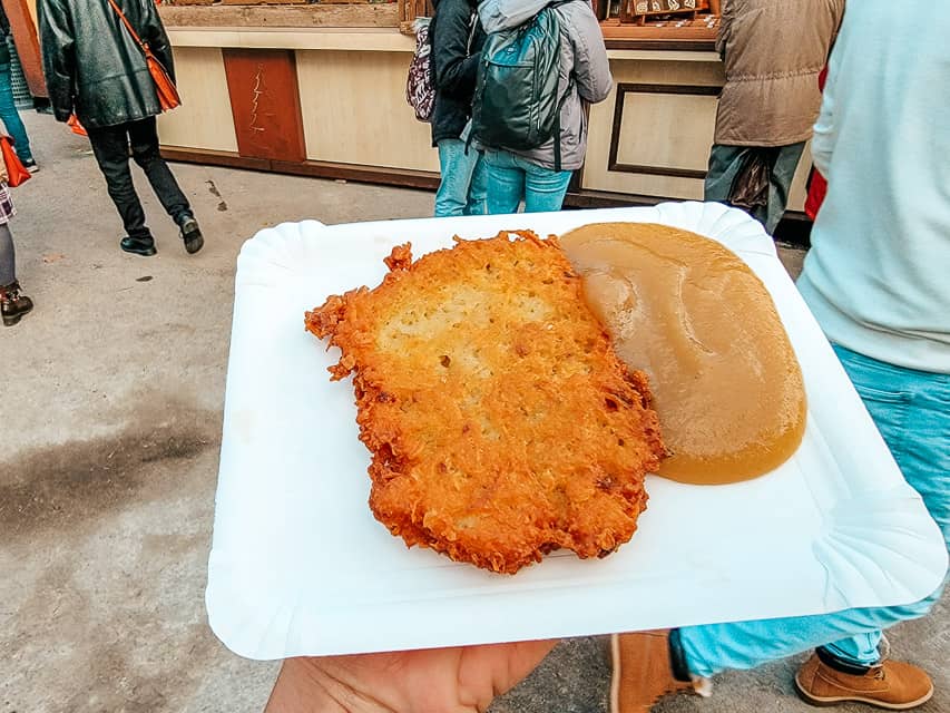A plate holding Reibekuchen - a fried potato cake, with applesauce next to it.