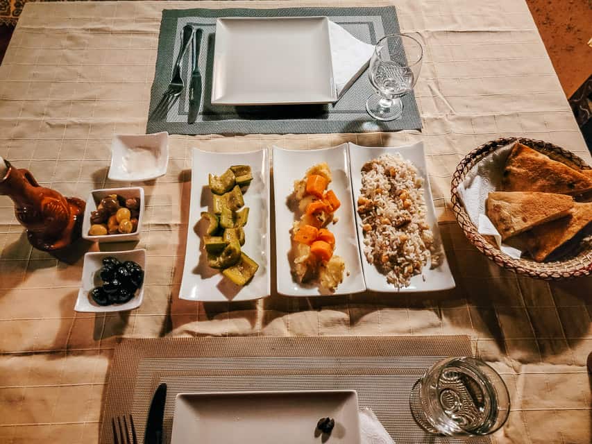 A variety of Moroccan appetizers are served consisting of olives, various vegetables, rice, and flat bread.