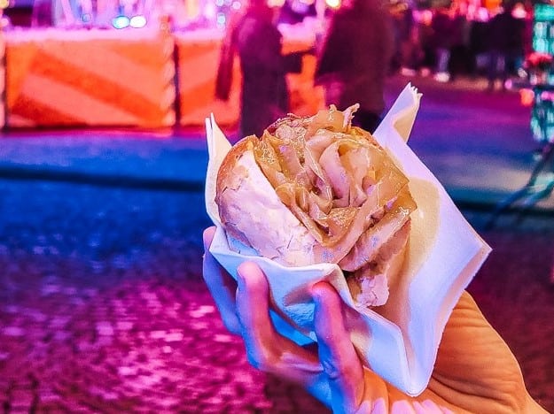 a hand holds a sandwich with a crusty bun and shaved meats inside.