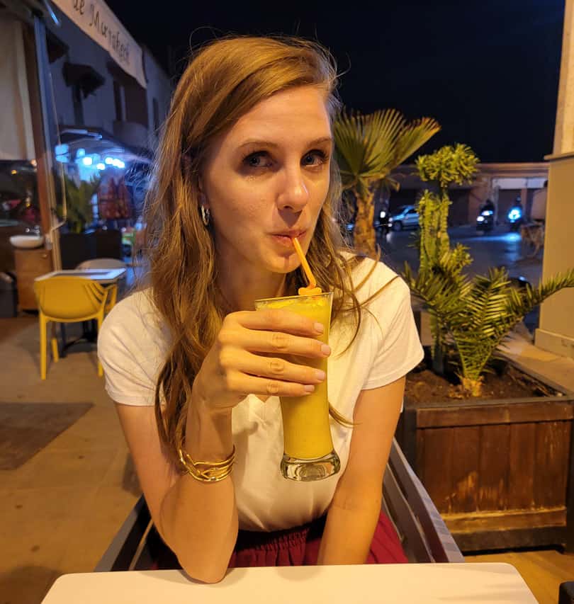 A woman drinks a glass of fruit juice in a Moroccan plaza at night.