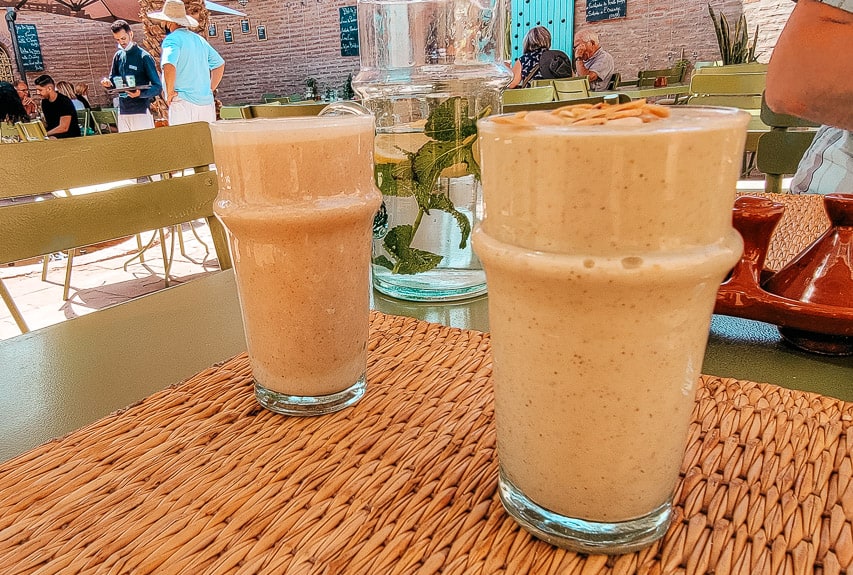 Two glasses rich smoothies. One has avocado, dates, and almond milk. The other is milk, dates, and orange blossom.