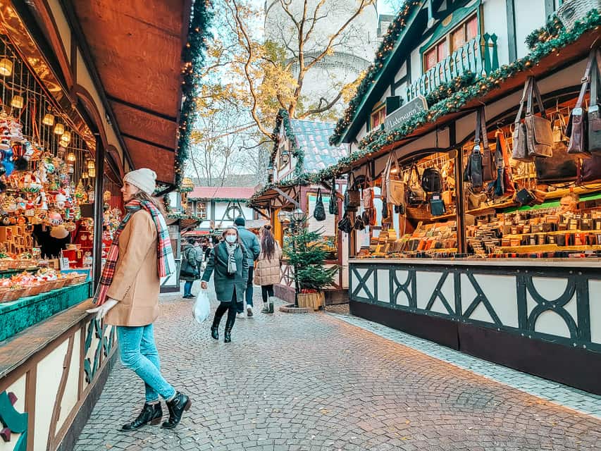 A row of St. Nicolas market - bricked lane, timbered stalls lined with greenery, and stalls filled iwth ornaments, and leather goods.