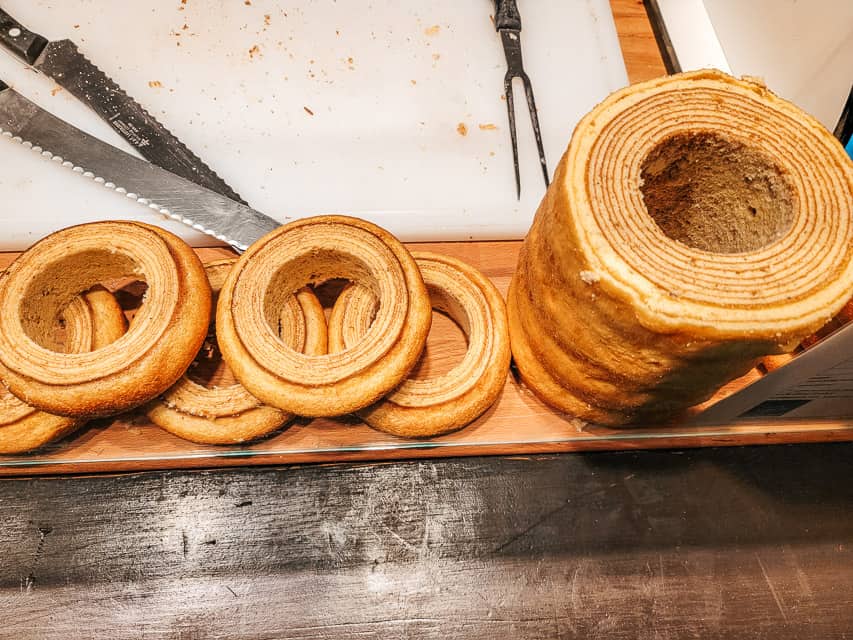 A platter of tree bread in a market stall, with the dessert cut so you can see the layers and rings the batter made.