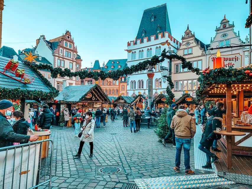 People mill about the Trier Christmas market, with stalls situated in a circle on the cobblestoned road of the main square in Trier.