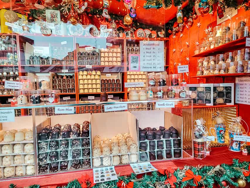 A market stall with stacks of chocolate covered marshmallow mousse balls, in a variety of flavors.
