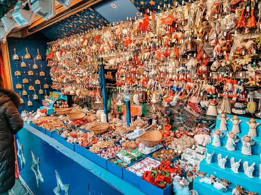 A blue market stall covered racks of Christmas ornaments, in colors of red, gold, and tan.