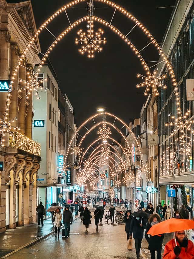 Large, pointed arches with stars hanging from them are hung between buildings on Freie Strasse street in Basel - you can see arches all the way down the street.