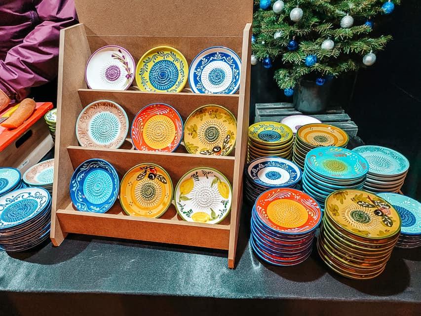 A stall at the market selling small, colorful plates with a grating fixture on it.
