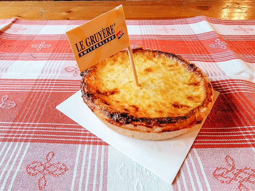 A baked cheese tart about the size of your hand sits on a red and white checked tablecloth.