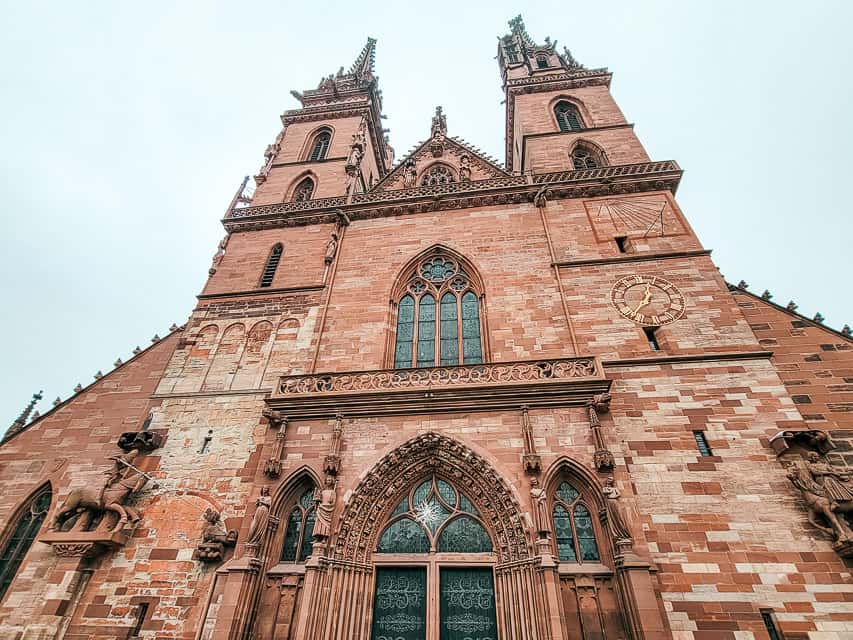 A view from the base of the Minster Basel Cathedral, loooking up to the spires. The cathedral is made of red brick and has two pointed spires.