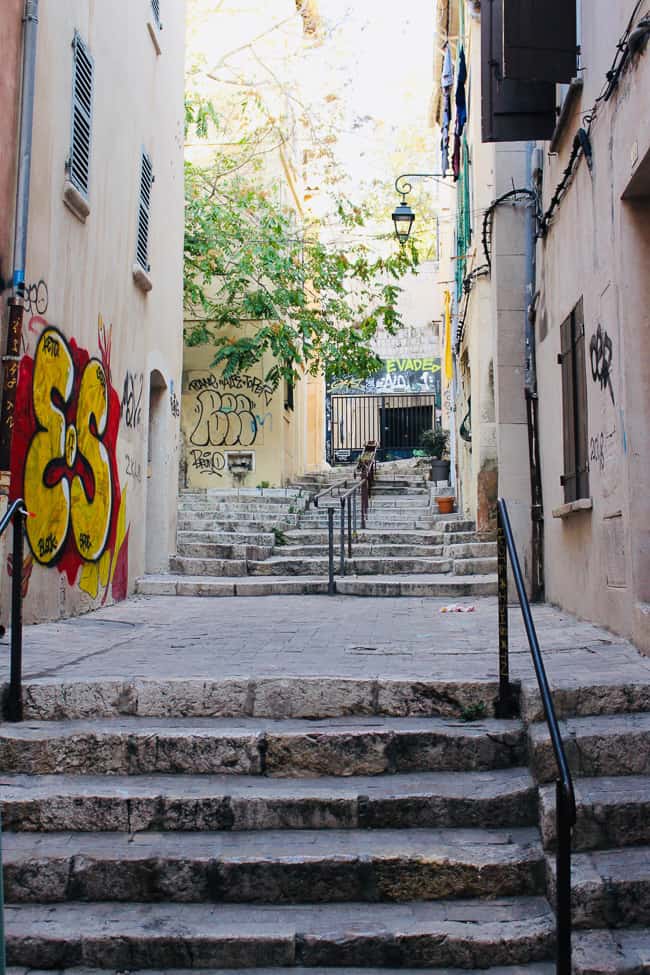 An alley with lots of graffiti leading up the stone staircases and trees.