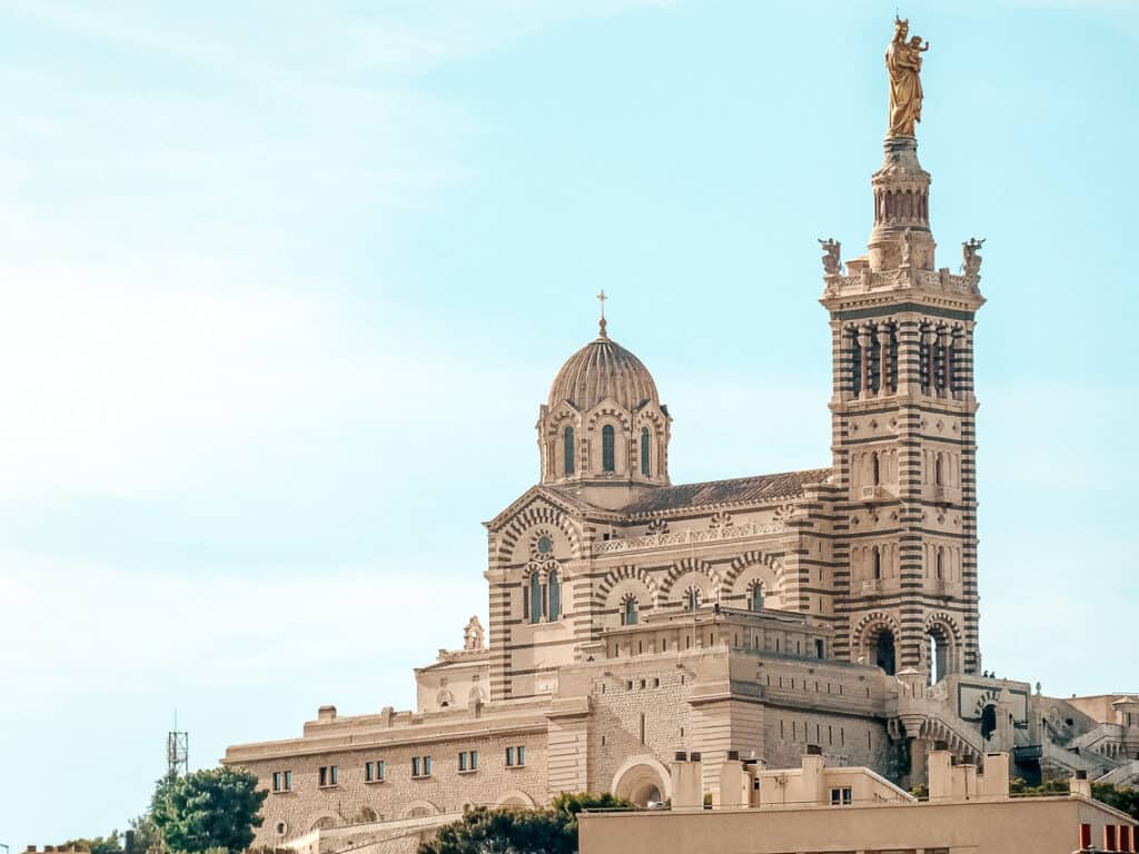 A gorgeous stone church with intricate gargoyles and paintings on the outside on the edge of land next to the sea.