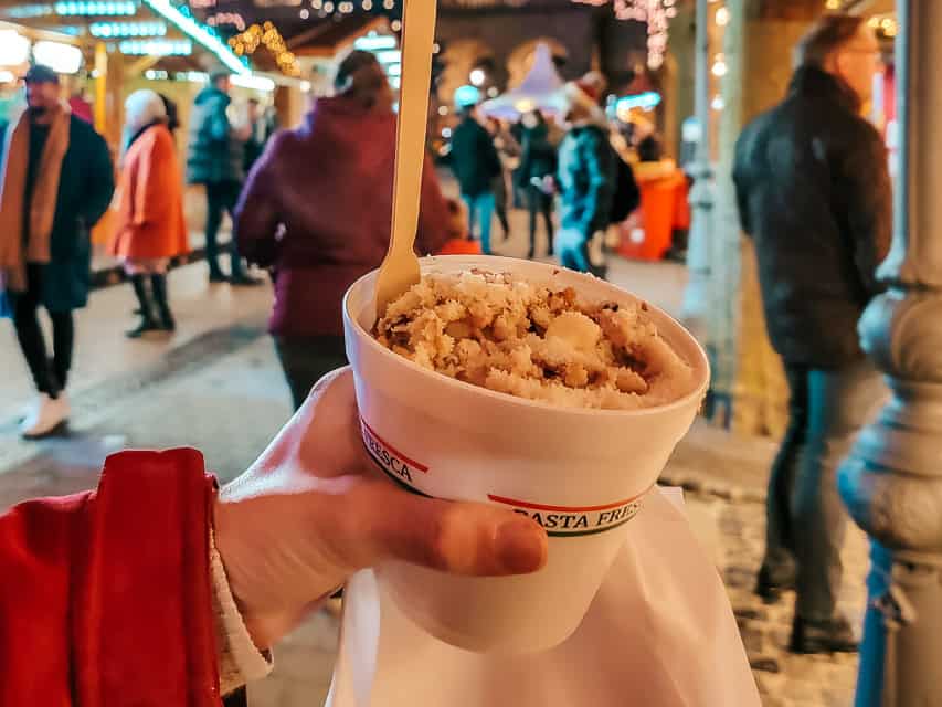 A styrofoam bowl holds spaetzle, a German noodle, with carbonara sauce, with the Luxembourg Christmas market in the background.