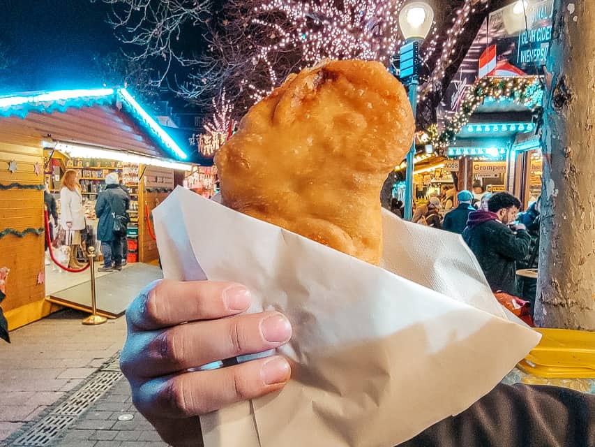 a hand holds up a calzone in the market.