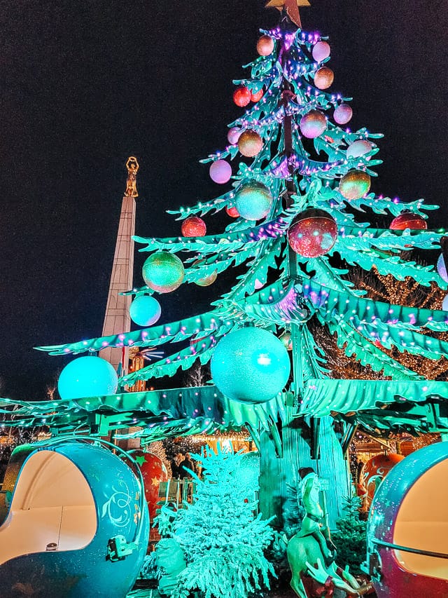A ride at the Place de la Constitution market that looks like a very tall Christmas tree, and the round ornaments on the bottom of the tree are open and have places for people to sit in them, and the tree spins.